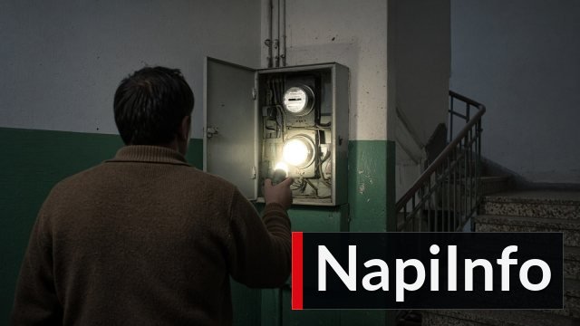 Egy lakó háttal állva zseblámpával világítja meg a villanyórát egy panelház lépcsőházának nyitott mérőszekrényében.